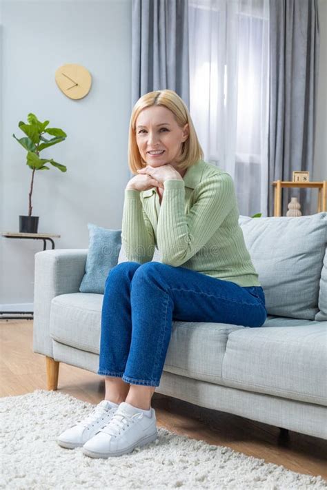 Pretty Mid Aged Blonde Woman Sitting On The Sofa And Looking Contented Stock Photo Image Of