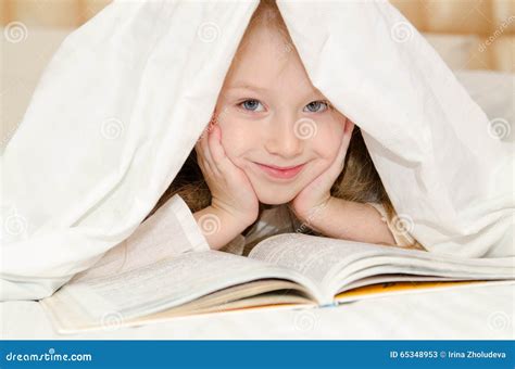 Petite Fille Se Trouvant Sur Le Lit Et Lisant Un Livre Image Stock