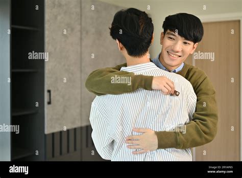 Happy Smiling Gay Couple With Keys Celebrating Moving Into New Home And Hugging Each Other