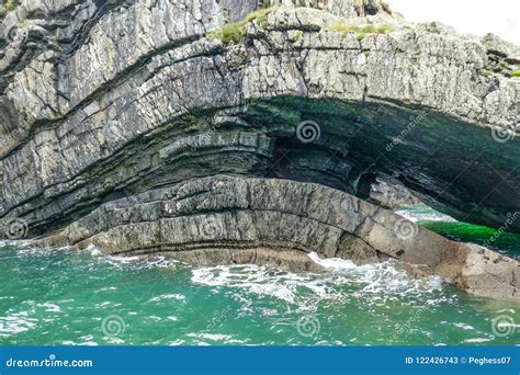 Dramatic Coastal Cliff Rock Layers Curve Forming Cave In Teal Aqua