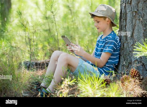 Boy Leaning Against Tree Trunk Using Digital Tablet Stock Photo Alamy