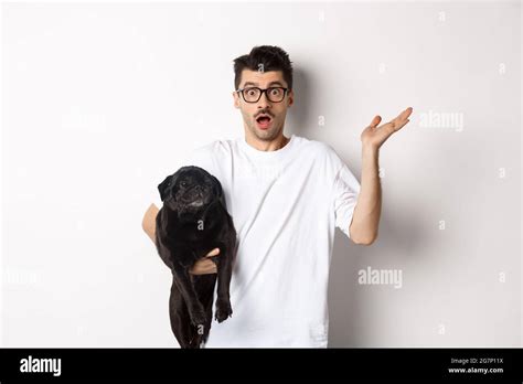 Image of confused hipster man holding dog and shrugging, dont know ... 