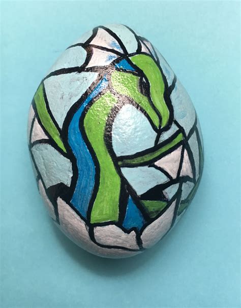 A Painted Rock Sitting On Top Of A Blue Surface With A Green And White