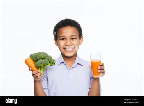 African American Boy holds carrot, broccoli, and carrot juice, on white ...