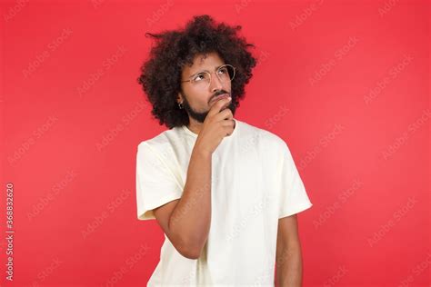 Shot Of Contemplative Thoughtful Young Man Keeps Hand Under Chin Looks