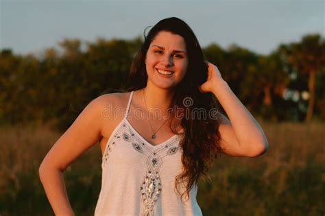 Attractive Long Curly Haired Brunette Female Model Posing And Smiling For The Camera Outside