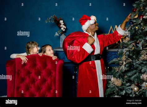 Santa Putting Ts Under Christmas Tree In Cozy Blue Room African