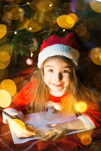 Niña con un gorro de papá noel y un vestido rojo debajo del árbol de