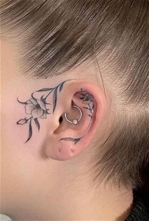 A Woman With Tattoos On Her Ear And Behind The Ear Is A Small Flower Tattoo