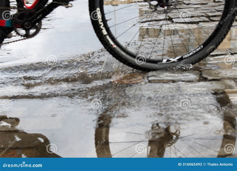 The Reflection Of Cyclists Is Seen In A Puddle Of Water Before The