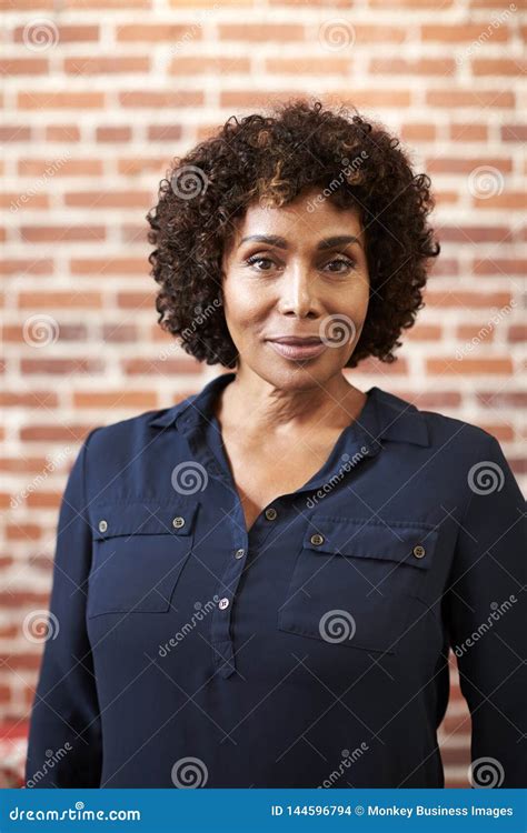 Portrait Of Smiling Mature Businesswoman Standing Against Brick Wall In Modern Office Stockfoto