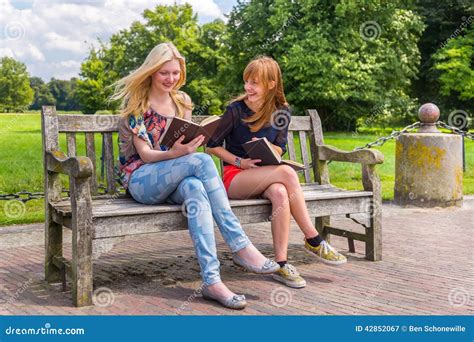 Meninas Que Sentam Se No Banco De Madeira Em Livros De Leitura Do