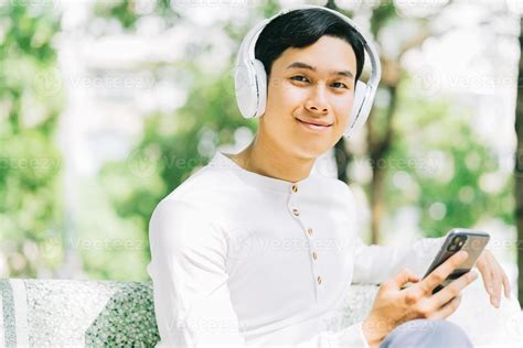 Handsome Asian Man Is Using His Phone To Listen To Music In The Park