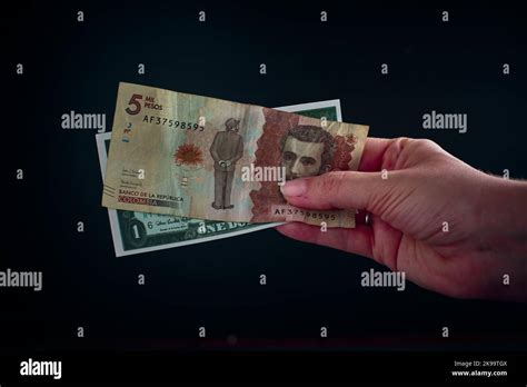 A hand holding a bill of 5 thousand Colombian pesos with 1 American ...