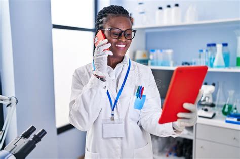 African American Woman Scientist Talking On Smartphone Using Touchpad