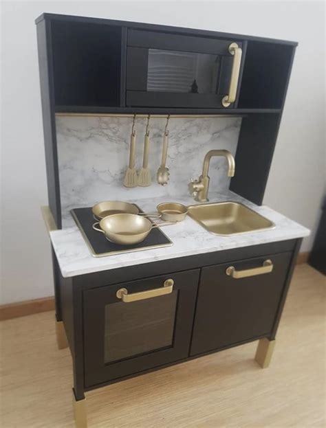 A Toy Kitchen With Black Cabinets And White Marble Counter Tops Gold