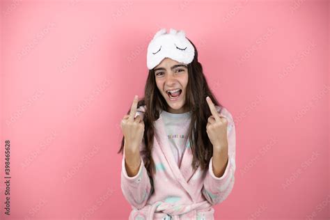 Pretty Girl Wearing Pajamas And Sleep Mask Over Pink Background Showing Middle Finger Doing Fuck