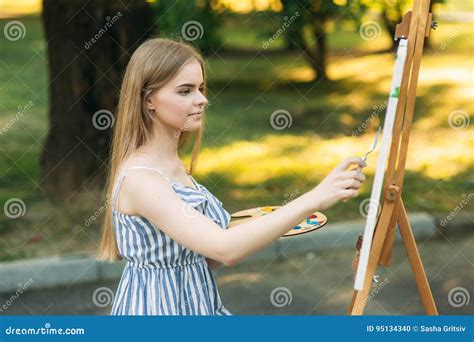 La Muchacha Del Blonde Pinta Una Pintura En La Lona Con La Ayuda De Las Pinturas Un Caballete De