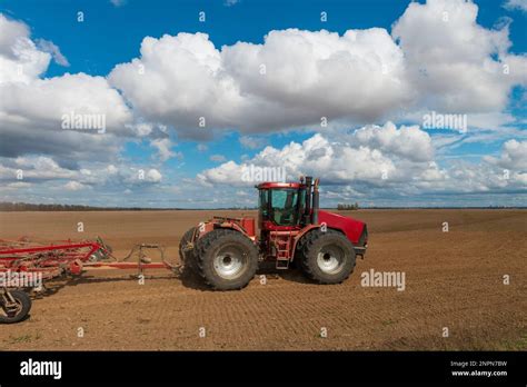 Red tractor plows fresh soil in a sunny spring day. Seasonal work on ...