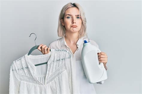 Jeune fille blonde tenant une bouteille de détergent et une chemise déprimée et inquiète pour la