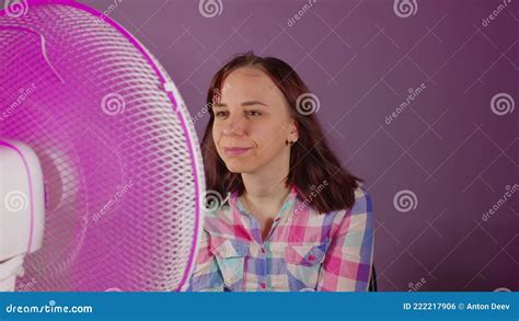 Acercamiento De Una Joven Sentada En Una Silla Frente A Un Ventilador Con Fondo Morado Brunette