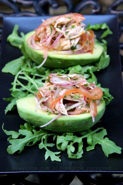 Two Avocado Halves Topped With Lettuce And Garnish On A Black Plate