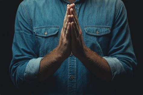 Man Stands Against Dark Background With Hands Clasped Together In