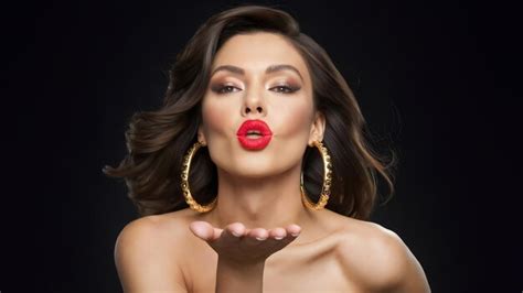 Passionate Brunette With Bright Lipstick And In Gold Massive Earrings Blowing Air Kiss On Black