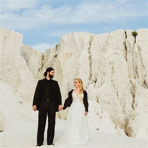 A Bride And Groom Holding Hands While Standing In Front Of Some White