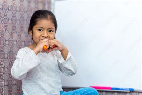 Niña latina sonriente y feliz escribiendo en la pizarra de clases con plumones de colores