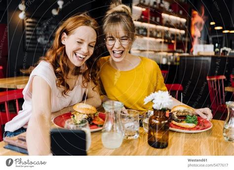 Zwei glückliche Freundinnen essen einen Burger und machen ein Selfie in