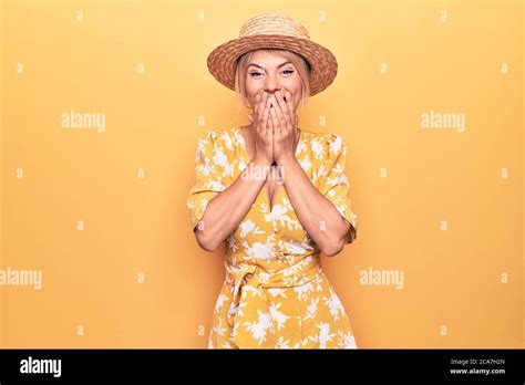 Beautiful Blonde Woman On Vacation Wearing Summer Hat And Dress Over Yellow Background Laughing