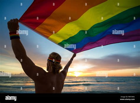 Man Holding A Fluttering Rainbow Gay Pride Flag On Beach At Sunrise Stock Photo Alamy