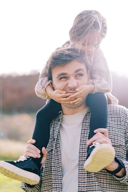 Premium Photo Little Smiling Girl Covered Her Dad Mouth With Her Palms While Sitting On His