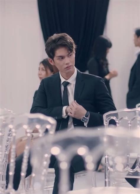 A Man In A Suit And Tie Sitting At A Table With Many Chairs Around Him