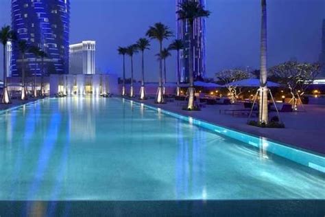 an empty swimming pool with palm trees and buildings in the background ...