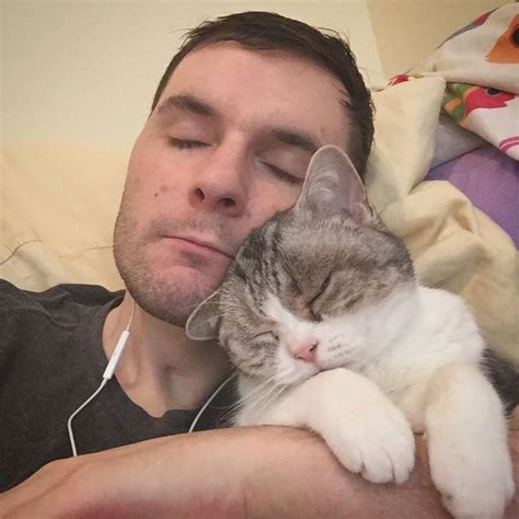 A Man Laying In Bed With His Head Resting On A Cat S Earphones