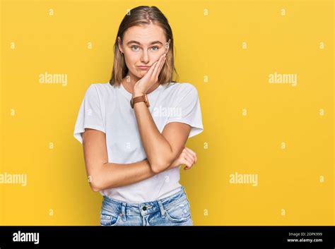 Belle jeune femme blonde portant décontracté t shirt blanc pensant fatigué et ennuyé avec des