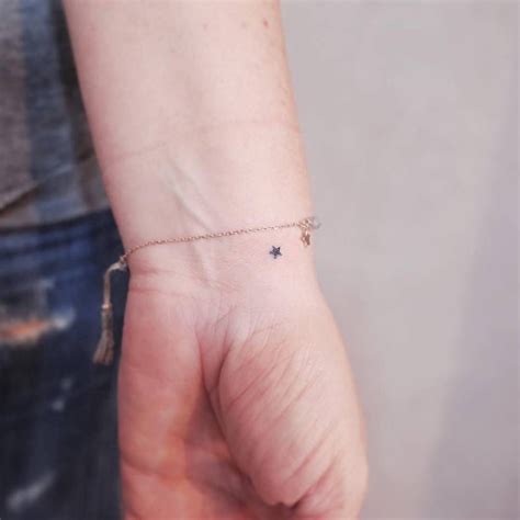 A Person Wearing A Tiny Star Tattoo On Their Left Wrist With A Tassel