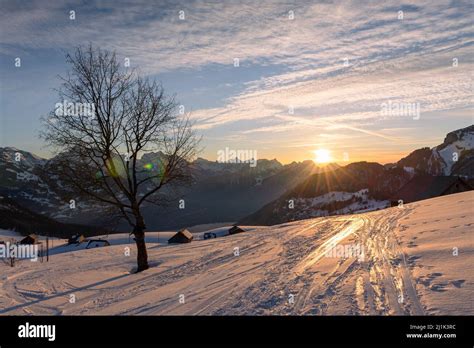 Snow Covered Mountain Meadows With Hay Huts In Front Of The Panorama Of