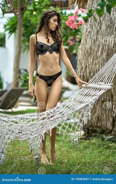 Brunette Woman In Dark Lingerie Posing Near Wicker Hammock Outdoors