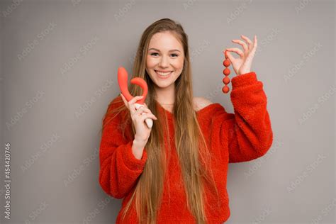 An Attractive Girl In A Sweater Depicts The Emotion Of Happiness Smiling Holding A Red Dildo