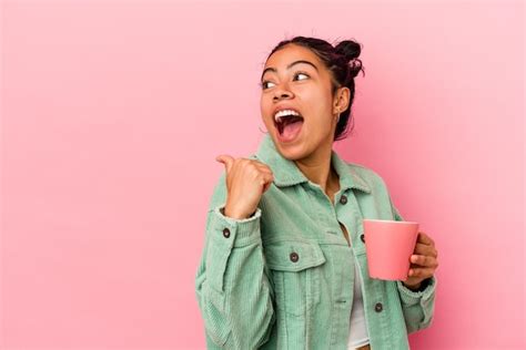 Joven Latina Sosteniendo Una Taza Aislada En Puntos De Fondo Rosa Con El Dedo Pulgar Lejos