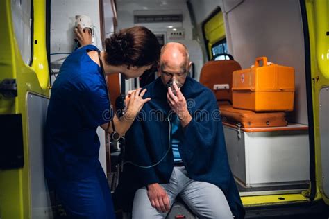 Woman In Medical Uniform Stands With Man Who Sits In Oxygen Mask In