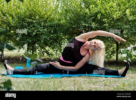 Positive Blonde Woman Performs Stretching Exercise In The Park Fitness Outdoor Workout Stock