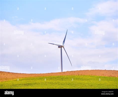 Wind Turbine Generating Electricity Between An Arid Field And A Blue