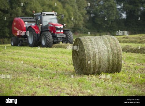 Round Bale Of Silage In Field With Tractor And Round Baler In