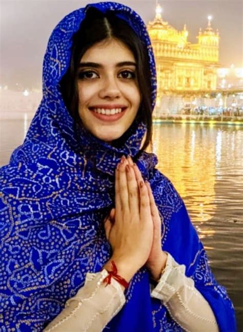 A Woman Wearing A Blue Shawl Standing In Front Of A Body Of Water