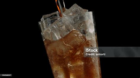 Pouring Cola Soda Into Glass Of Ice On A Black Background Stock Photo