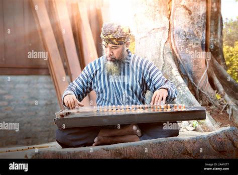 Asian old man playing kecapi with tree background. Kecapi is a ...